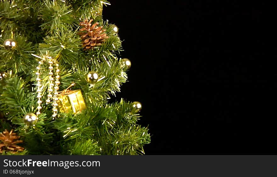 Green Christmas tree (part of) with gold ornaments rotates on a black background. Green Christmas tree (part of) with gold ornaments rotates on a black background