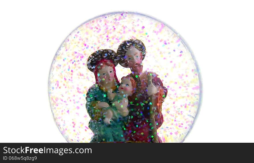 Joseph and Mary with baby Jesus in her arms. Glass ball with toy figures on a white background. The blizzard of multicolored sequins. Joseph and Mary with baby Jesus in her arms. Glass ball with toy figures on a white background. The blizzard of multicolored sequins