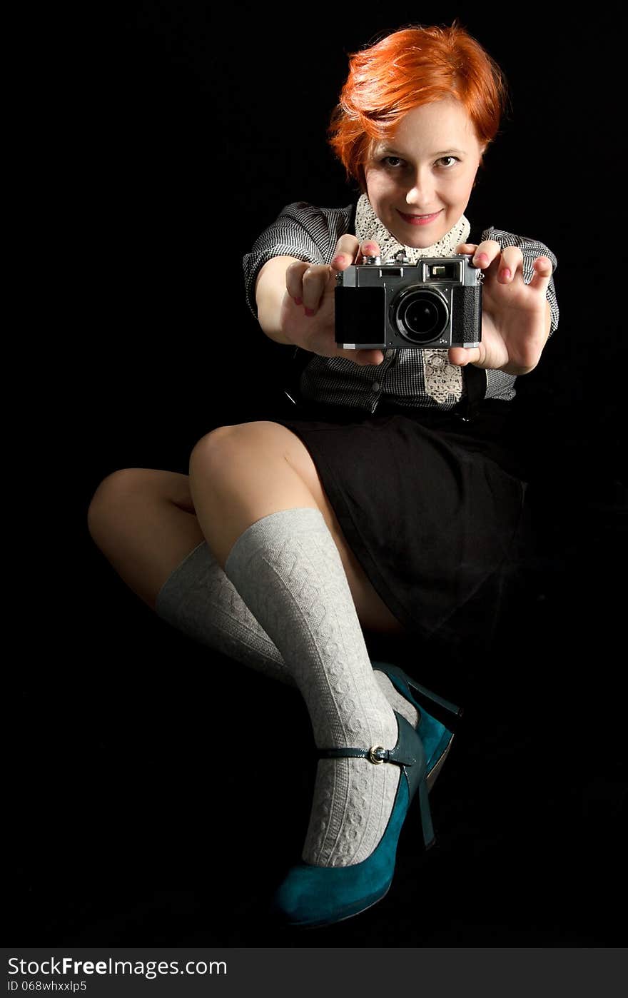 Red hair girl holding an old camera on black background. Red hair girl holding an old camera on black background