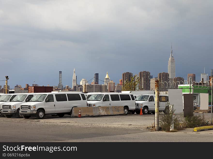 A parking lot with white vans infront of the New York City sky line on a cloudy afternoon. A parking lot with white vans infront of the New York City sky line on a cloudy afternoon.