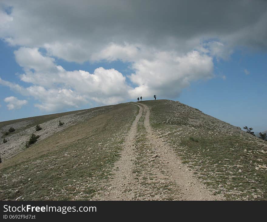 The road to the top of the mountain on the background of a contrasting sky with clouds. The road to the top of the mountain on the background of a contrasting sky with clouds