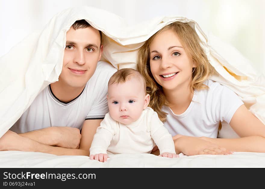 Happy family in bed under a blanket. mother, father, baby