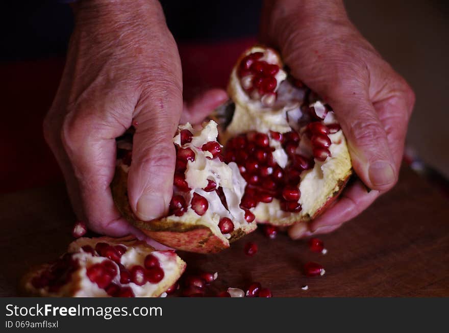 A man opens a pomegranate with its hand and the red seeds spread on the wooden table