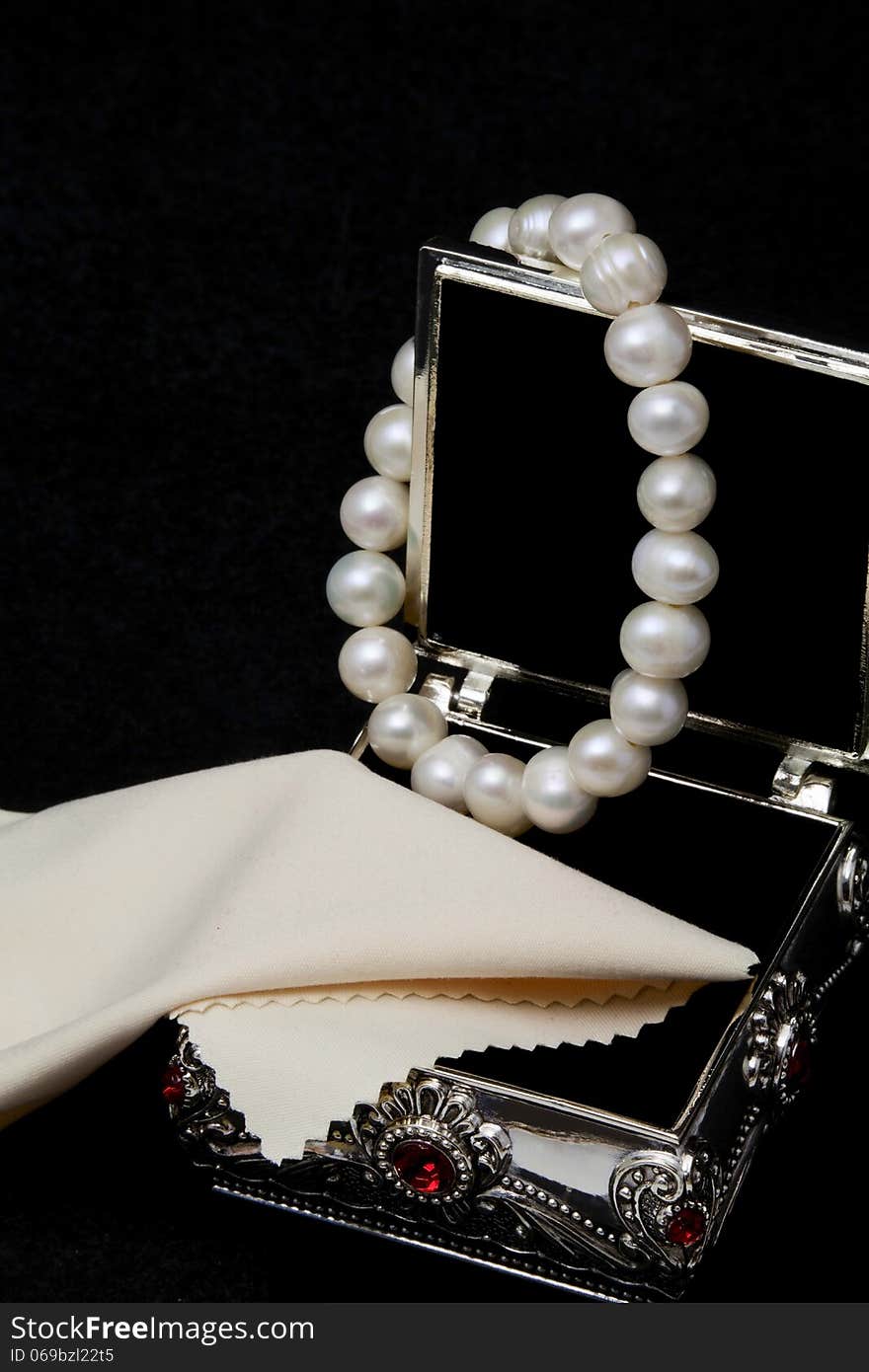 Pearl bracelet hanging on an open jewelry box on a black background