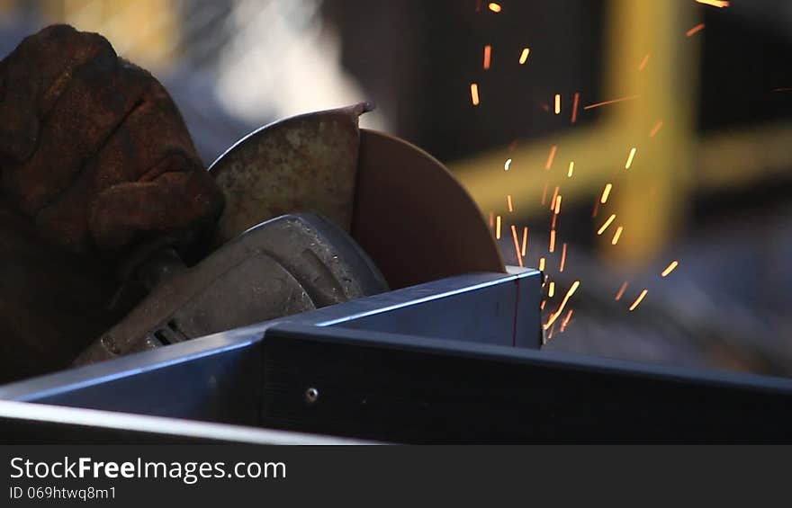 Worker sawing metal with electrical saw, grinder.