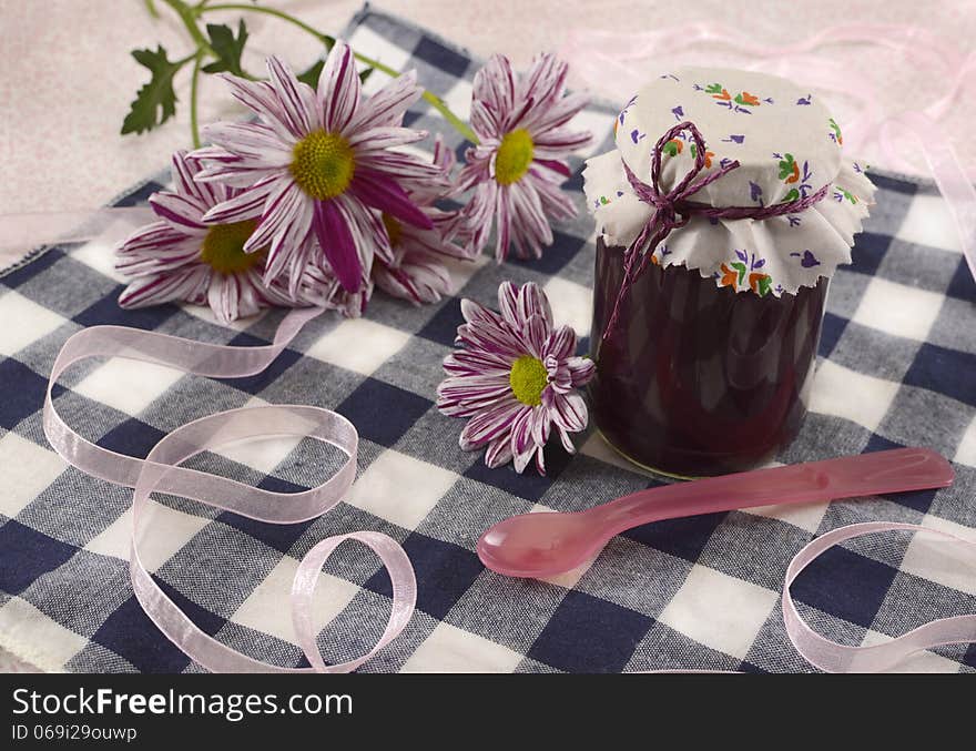 Jam jar with flowers and spoon on cute tablecloth