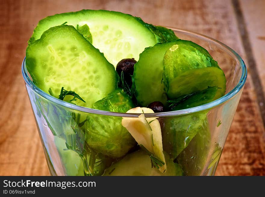 Appetizer with Slices of Delicious Pickled Cucumbers in Brine of Garlic, Dill, Parsley and Black Peppercorn in Glass Dish closeup on Wooden background