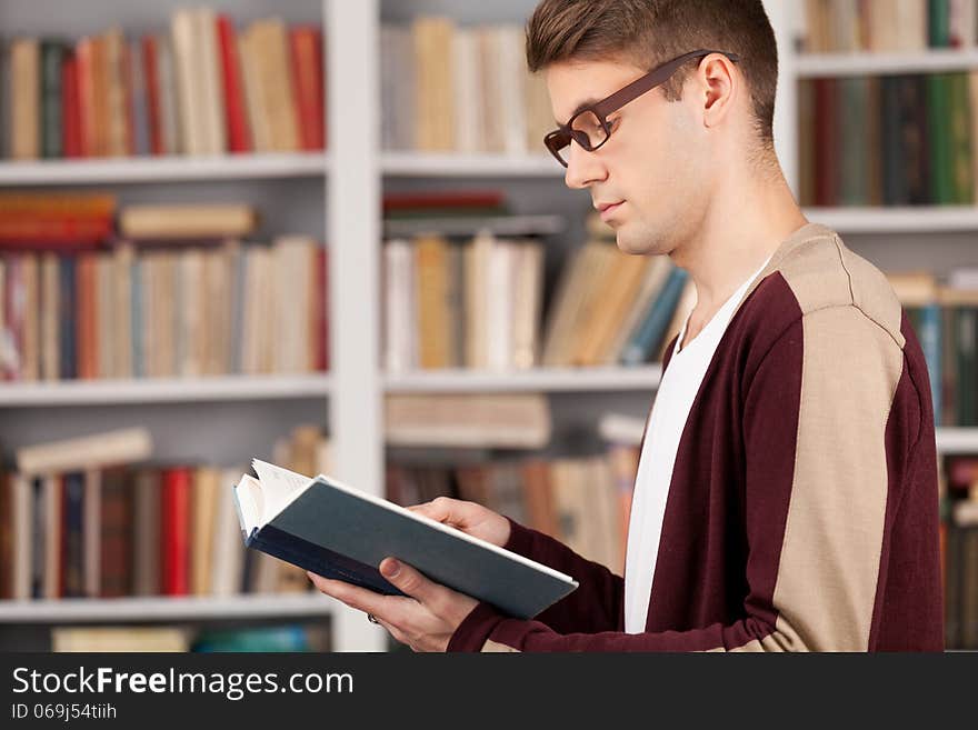 Side View of young man reading a book while standing at the library. Side View of young man reading a book while standing at the library