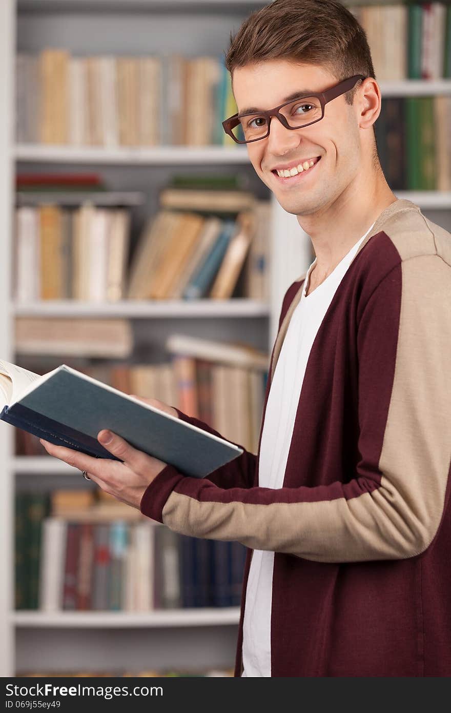 Side view of young man reading a book and smiling while standing at the library. Side view of young man reading a book and smiling while standing at the library