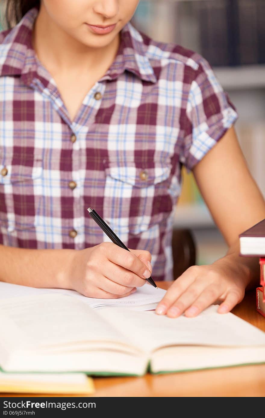 Young woman writing something in her note pad and reading book while sitting at the desk. Young woman writing something in her note pad and reading book while sitting at the desk