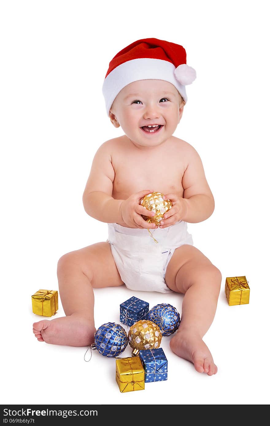 Little baby boy holding a bauble and wearing a red santa cap smiling and having fun with presents on the floor, isolated on white. Little baby boy holding a bauble and wearing a red santa cap smiling and having fun with presents on the floor, isolated on white