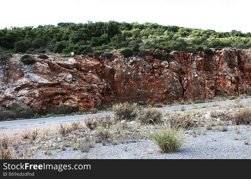 Its a road leading you through the Peloponnese. The rocky mountain stands out because of its red maroon color. Its a road leading you through the Peloponnese. The rocky mountain stands out because of its red maroon color.