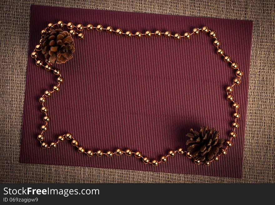 Horizontal blank greeting card. Light brown color linen background, claret paper, two pine cones and silver, golden color beads composition. Horizontal blank greeting card. Light brown color linen background, claret paper, two pine cones and silver, golden color beads composition.