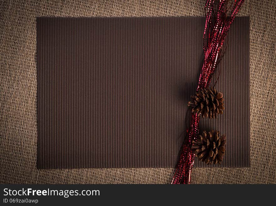 Horizontal blank greeting card. Light brown color linen background, claret paper, two pine cones and silver, golden color beads composition. Horizontal blank greeting card. Light brown color linen background, claret paper, two pine cones and silver, golden color beads composition.