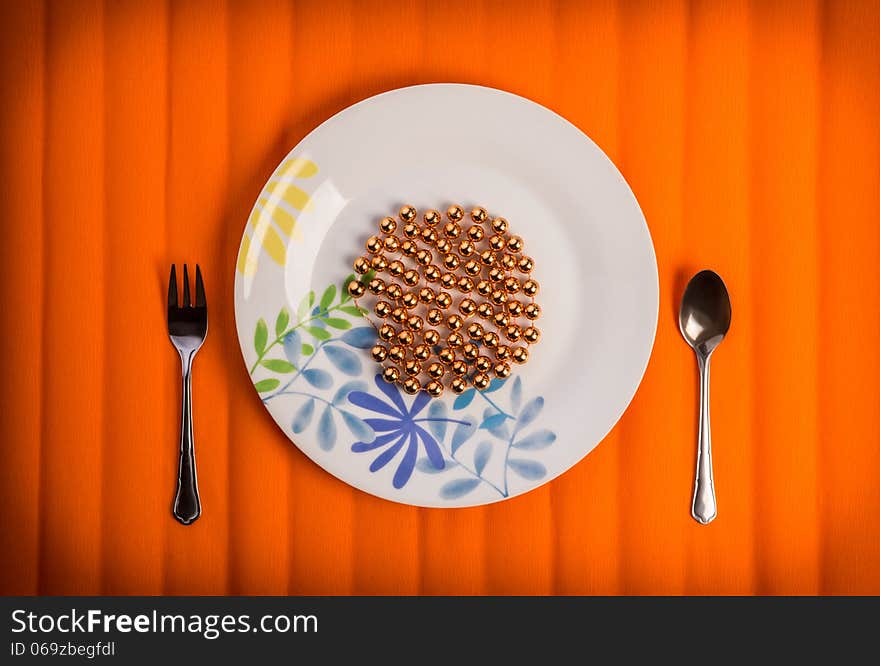 One lovely plate with golden beads on it , little fork and spoon by sides. Over textured bright orange color background. One lovely plate with golden beads on it , little fork and spoon by sides. Over textured bright orange color background.