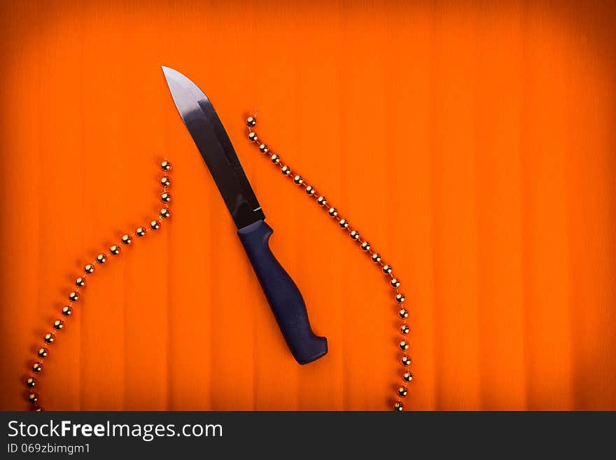 Knife cuts gold beads. Over textured bright orange color background.