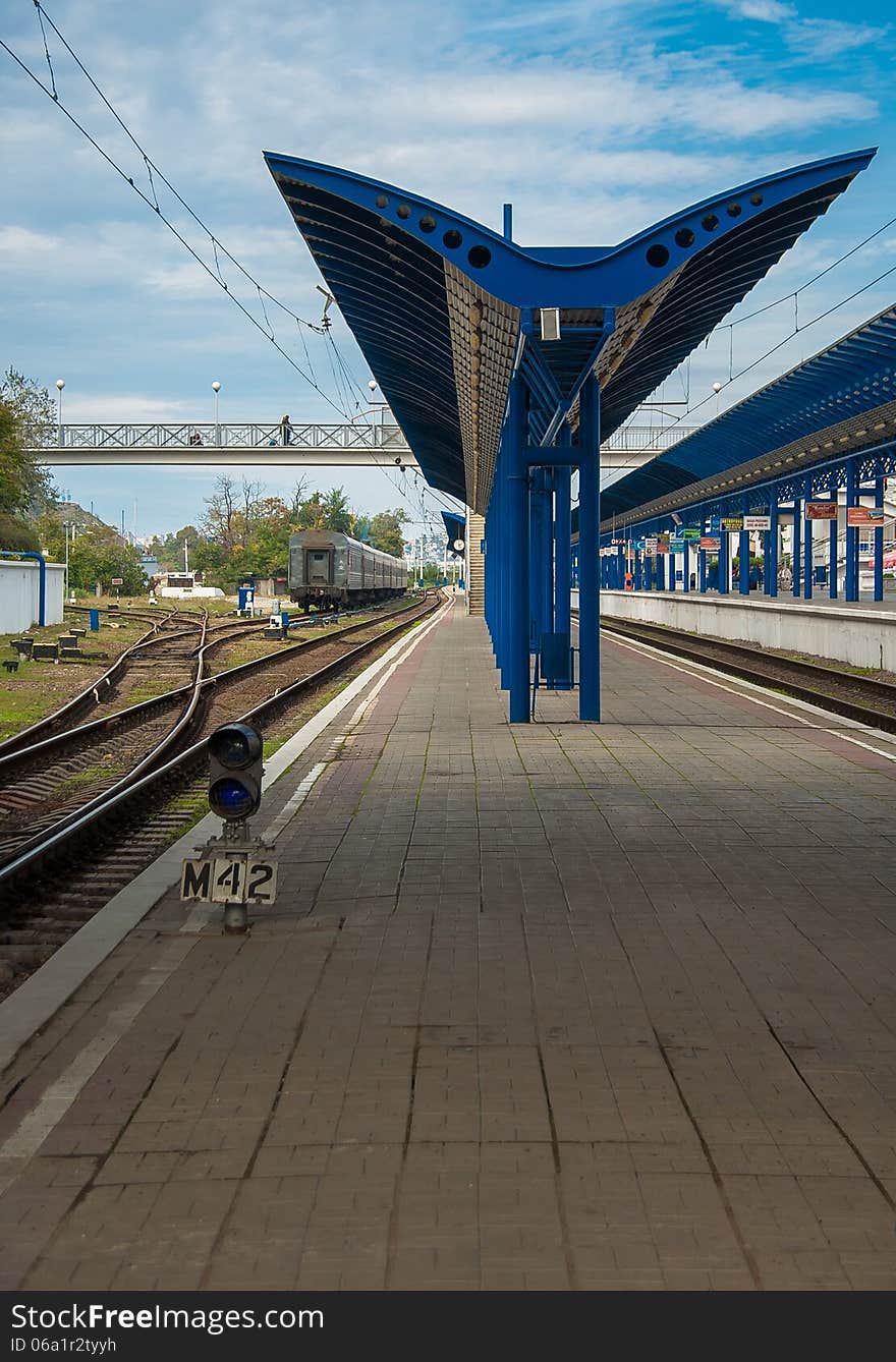 Railway platform and rails at the railway station without passengers and trains. Urban landscape - perspective way on a railroad. Crossing railroad tracks and blue signal lamp on a railway junction.