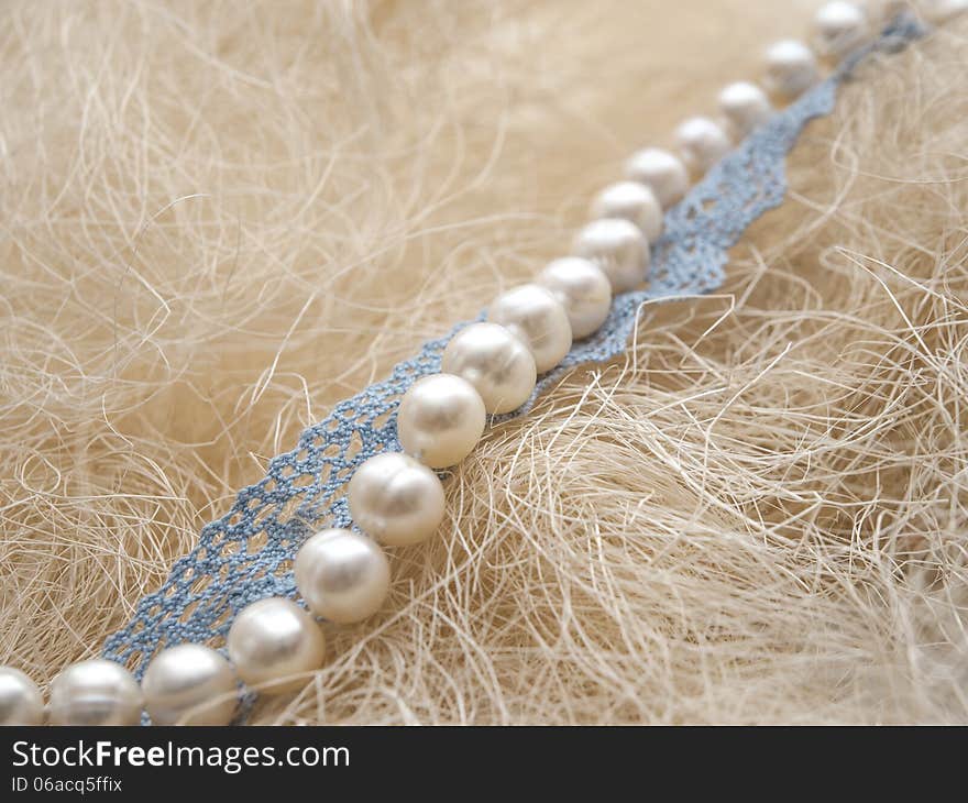 White pearl and blue handmade lace on straw background. White pearl and blue handmade lace on straw background