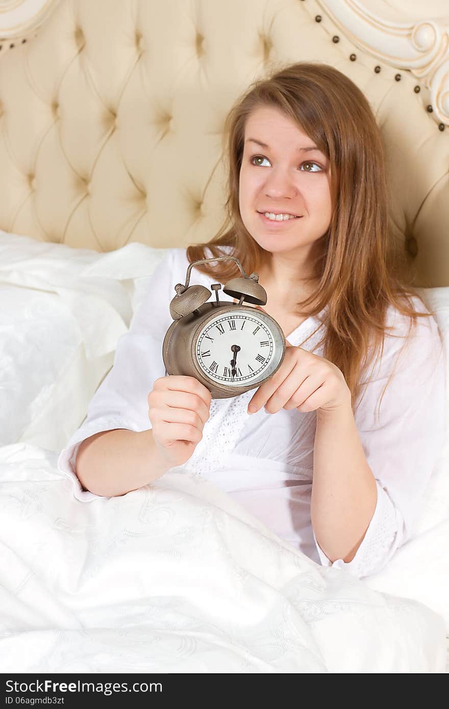 Young woman with alarmclock on the bed at the morning