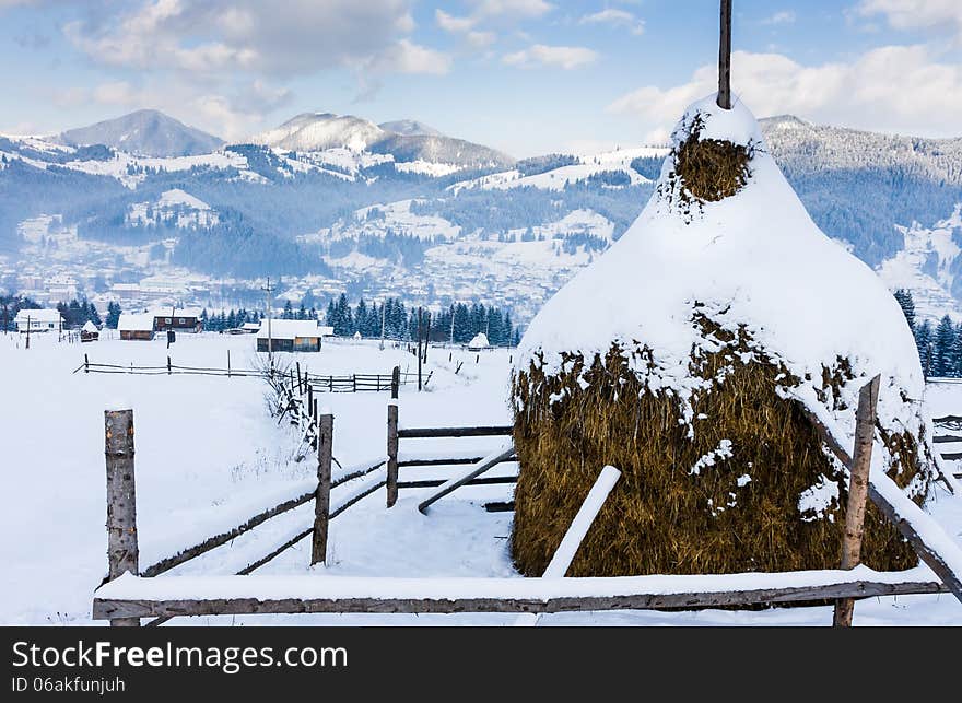 Snowy haystack on a background of a village in the mountains