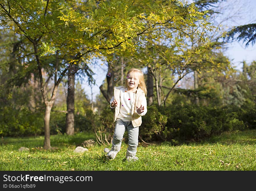 Funny little girl with soap bubbles in park