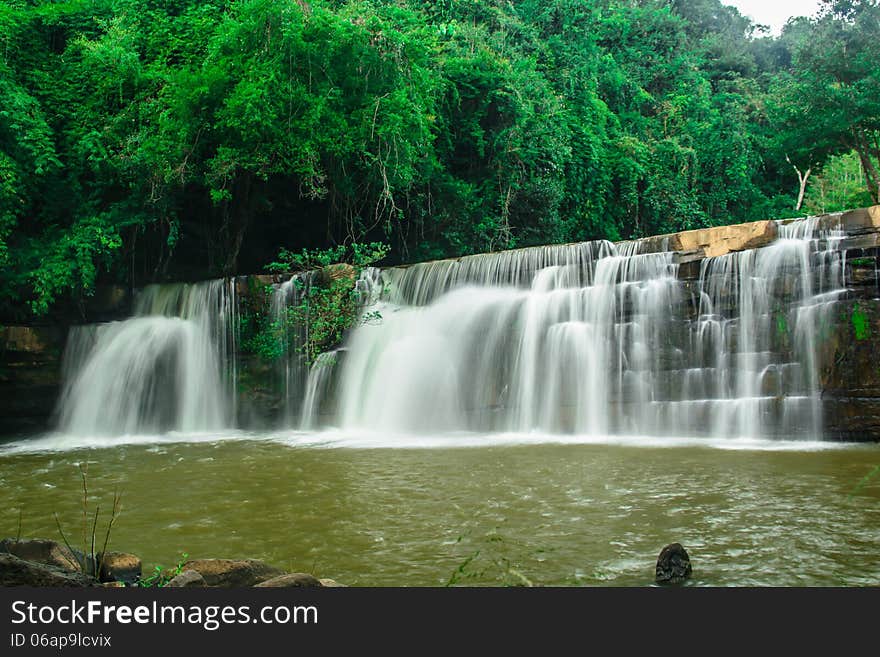 A beautiful waterfall with a green forest on the mountain