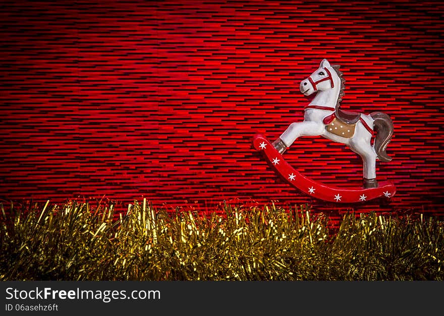 White color, rocking horse wooden toy over red color textured background with yellow sparkling garland at the bottom of composition. White color, rocking horse wooden toy over red color textured background with yellow sparkling garland at the bottom of composition.