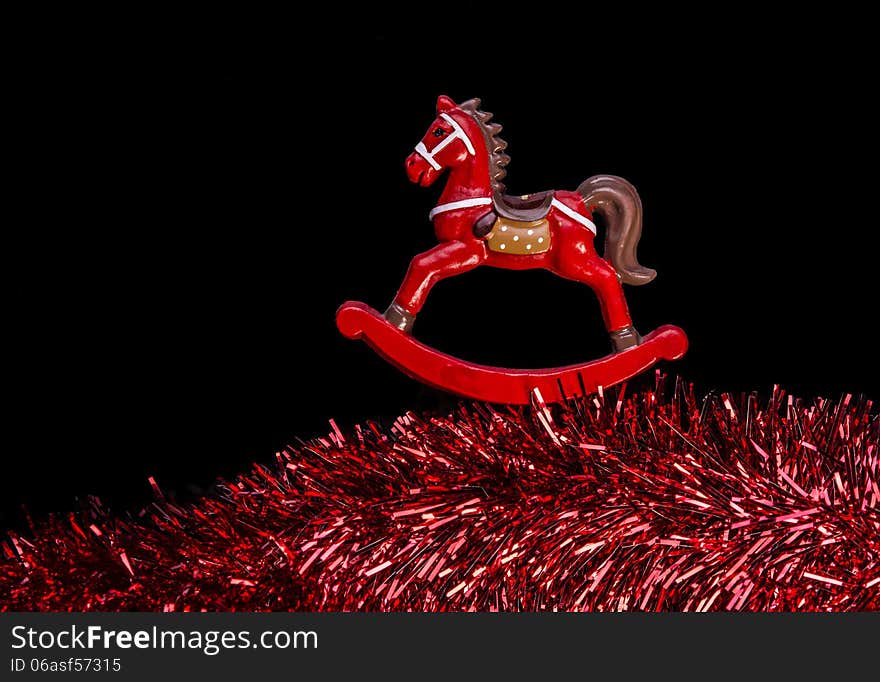 Red color rocking horse toy isolated over black color background, rocking above claret color textured sparkling garland at the bottom. Red color rocking horse toy isolated over black color background, rocking above claret color textured sparkling garland at the bottom.