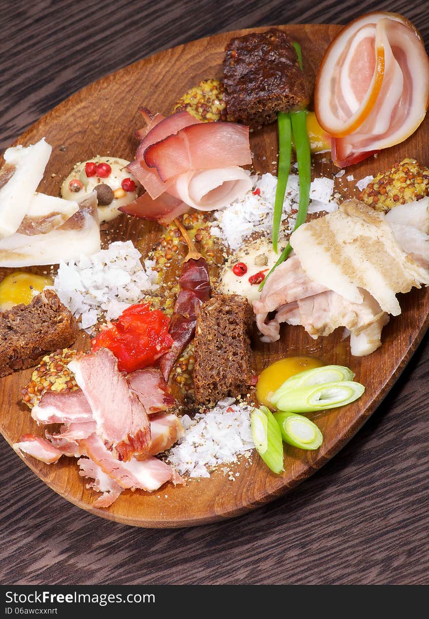 Wooden Plate with Various Smoked, Boiled and Uncooked Ham, Mustard, Salt, Brown Bread and Spices on Dark Wooden background. Wooden Plate with Various Smoked, Boiled and Uncooked Ham, Mustard, Salt, Brown Bread and Spices on Dark Wooden background