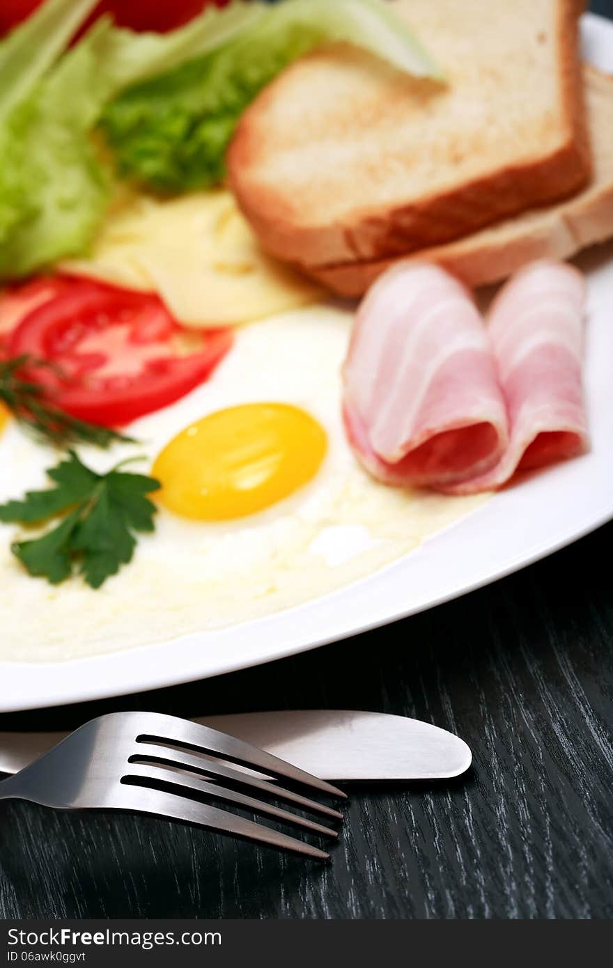 Closeup of fork and knife near plate with fried eggs, toasts and cheese