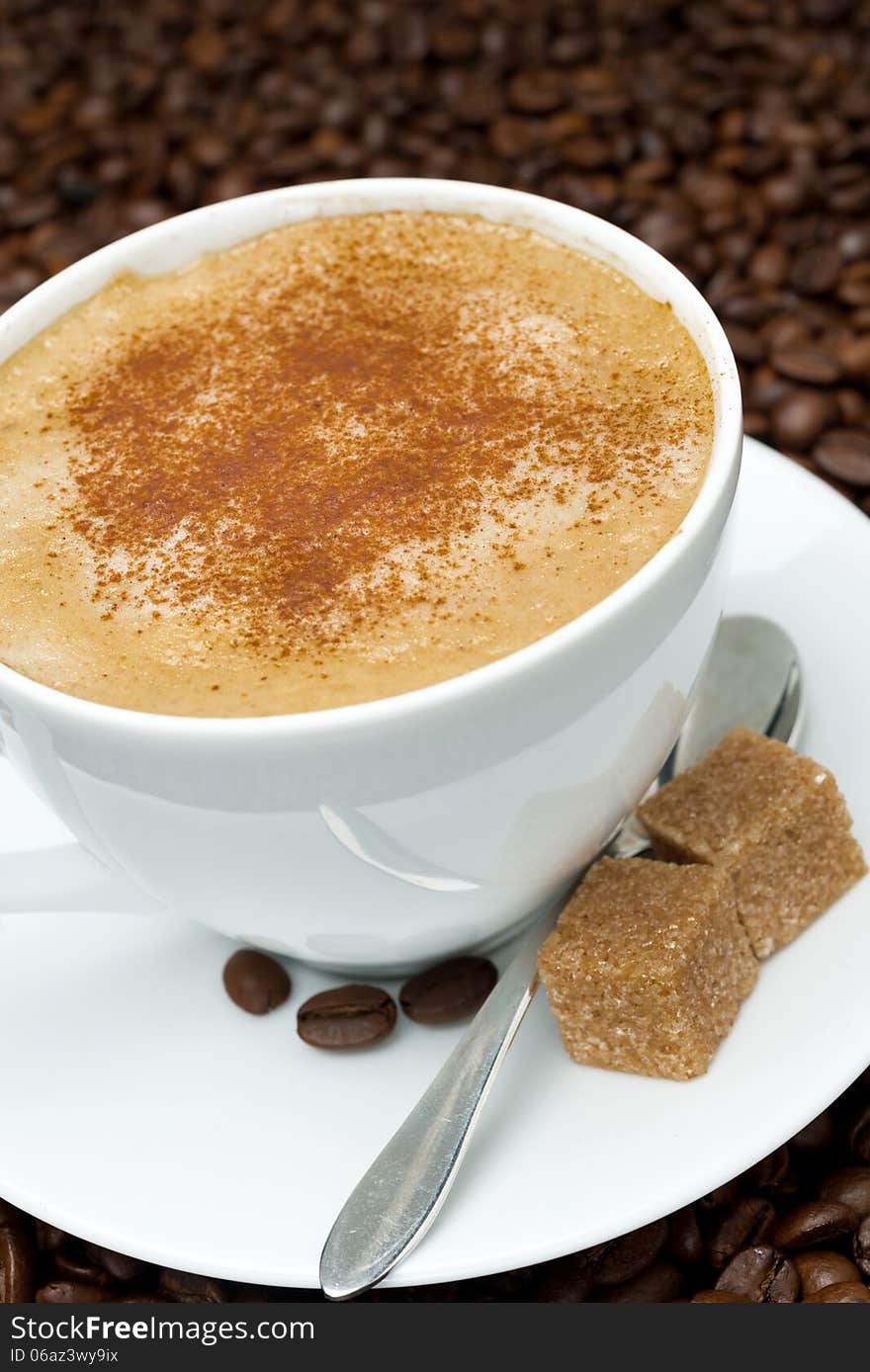 Cup of cappuccino with brown sugar on the background of coffee beans, close-up, vertical