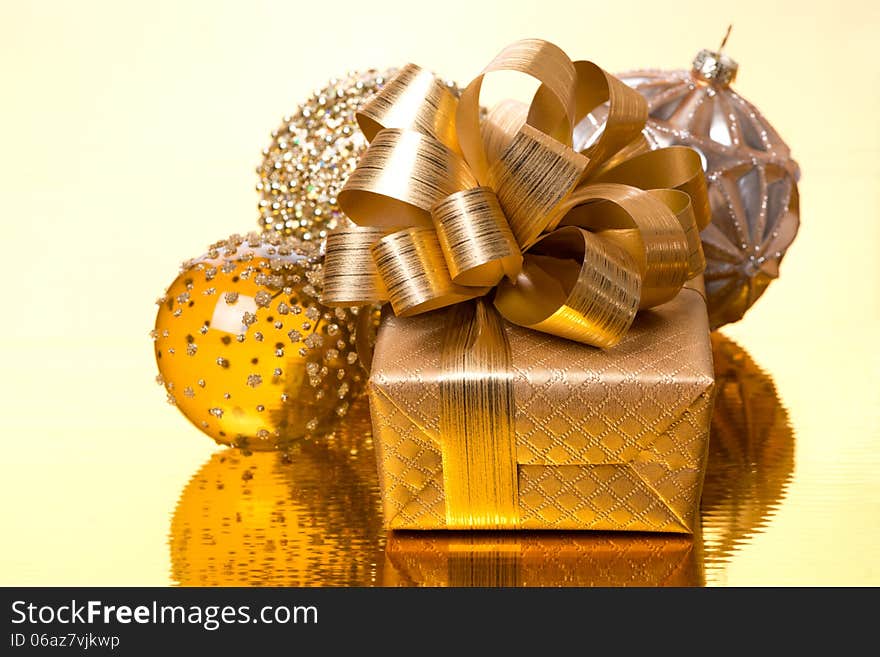 Gift box and Christmas balls on golden background, close-up