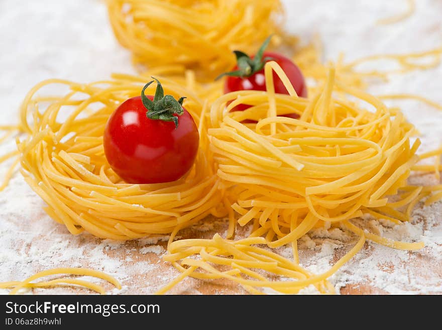 Italian egg pasta nest, cherry tomatoes on a cutting board sprinkled with flour, close-up. Italian egg pasta nest, cherry tomatoes on a cutting board sprinkled with flour, close-up