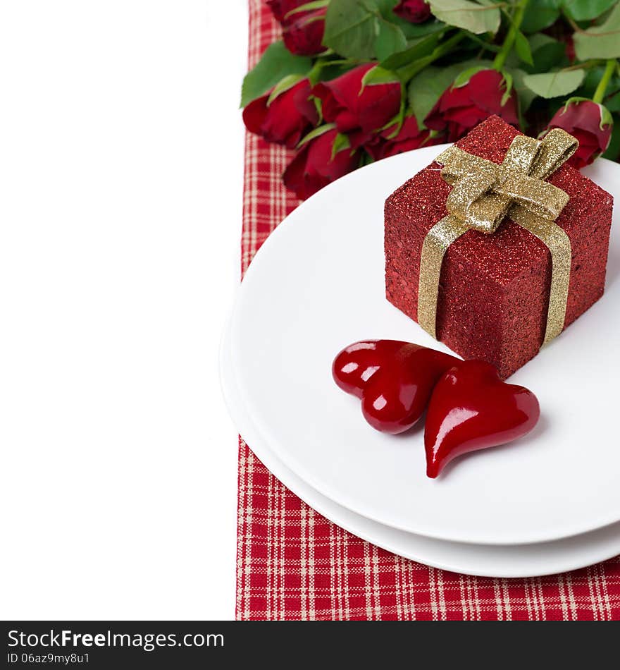 Red gift box and two hearts on a plate, roses in the background, isolated on white