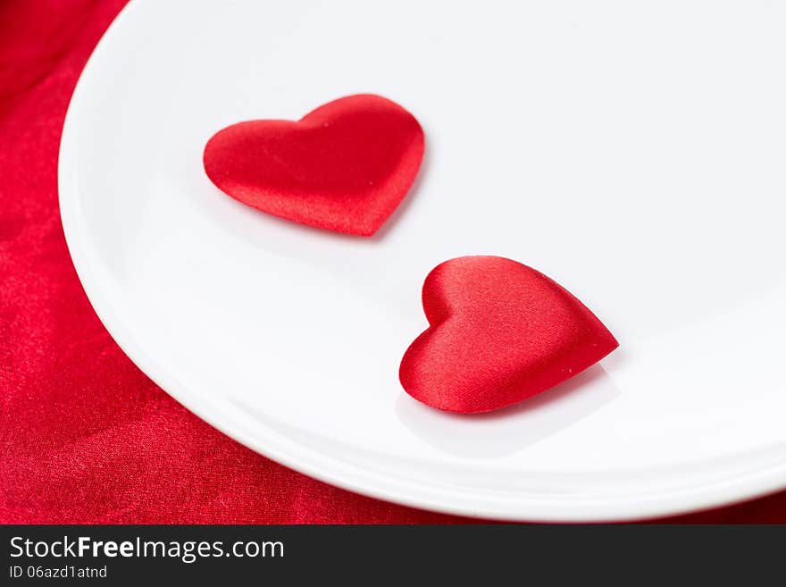 Two silk heart on a plate on red background, selective focus, close-up