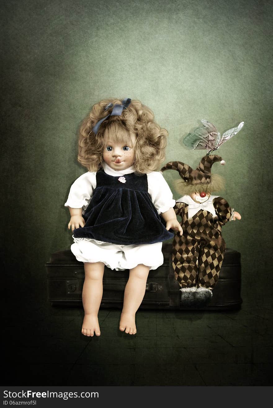 Doll and Clown are sitting on a suitcase on a vintage background. Doll and Clown are sitting on a suitcase on a vintage background