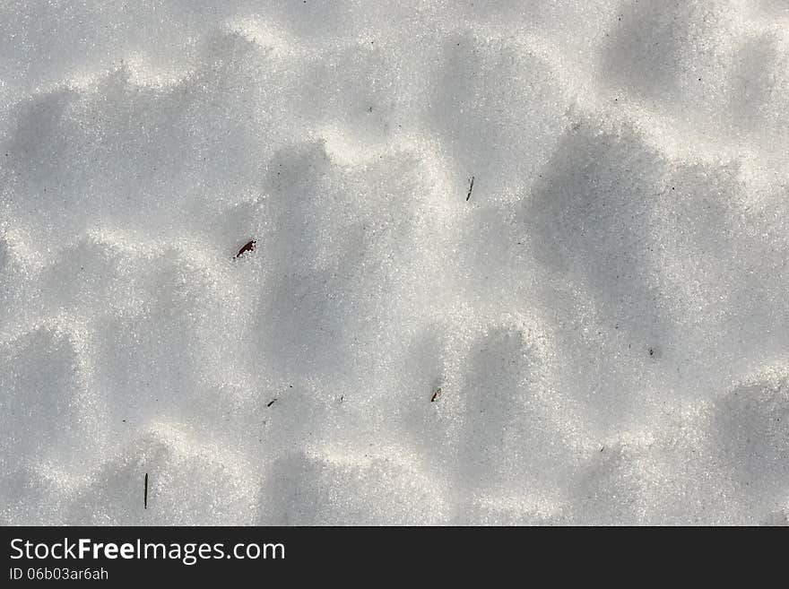 Shiny snow close up with shadows and small pieces of grass poking through. Shiny snow close up with shadows and small pieces of grass poking through