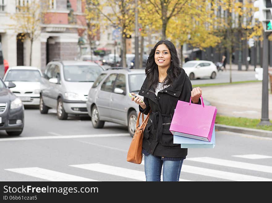 Beautiful smiling woman crossing street with shopping bags and p