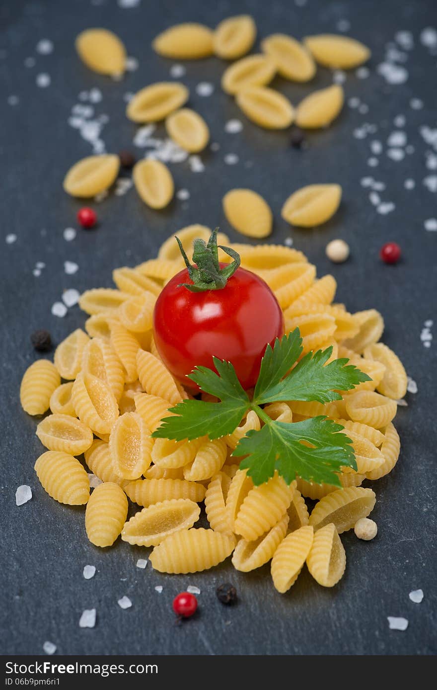 Italian pasta shells, cherry tomatoes, salt and pepper on a dark background, vertical