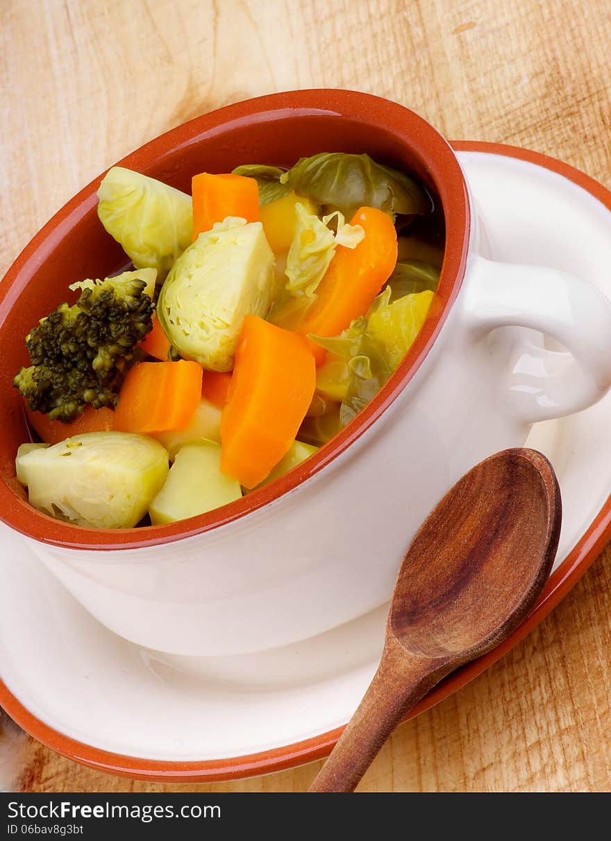 Rustic Vegetable Stew with Broccoli, Carrot, Leek and Potato in Beige Bowl with Wooden Spoon closeup on Wooden background. Rustic Vegetable Stew with Broccoli, Carrot, Leek and Potato in Beige Bowl with Wooden Spoon closeup on Wooden background