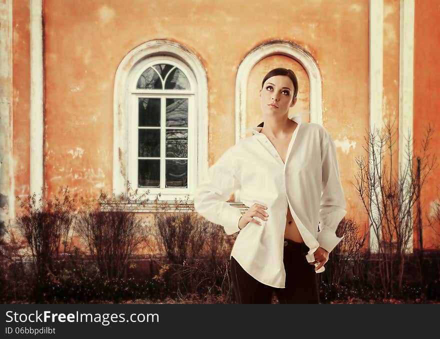 Circumspect woman. Young gorgeous lady in white man's shirt standing in a pose and looking up with thoughtful expression. Outdoors, vintage building wall as background. Circumspect woman. Young gorgeous lady in white man's shirt standing in a pose and looking up with thoughtful expression. Outdoors, vintage building wall as background.