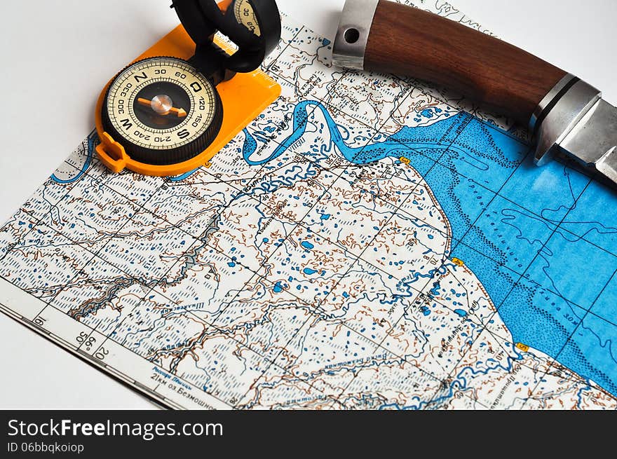 Outdoor compass in orange body with black lid and a mirror in it is over a topographic map. Outdoor compass in orange body with black lid and a mirror in it is over a topographic map.