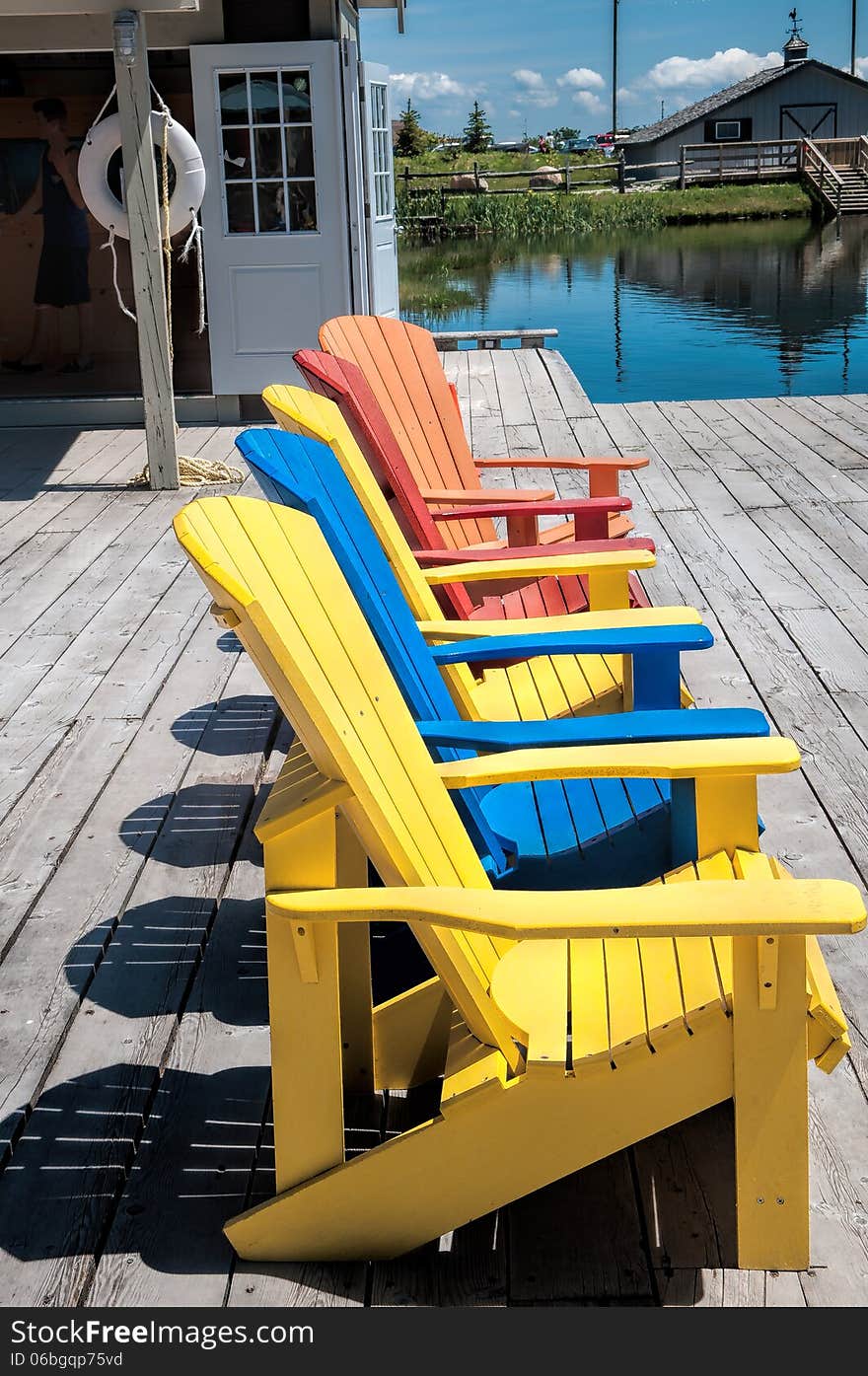 Wooden chairs of different colors on a wooden deck near the lake. Wooden chairs of different colors on a wooden deck near the lake