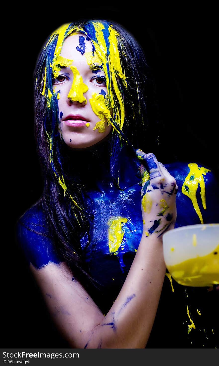 Beauty/fashion close up portrait of woman painted blue and yellow with brushes and paint  on black background