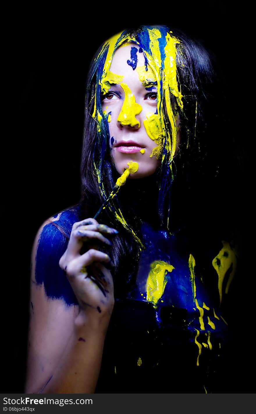 Beauty/fashion close up portrait of woman painted blue and yellow with brushes and paint  on black background