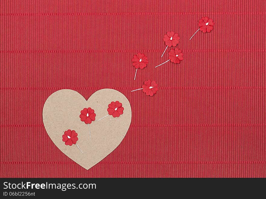 Cardboard heart with paper flowers on red corrugated background.