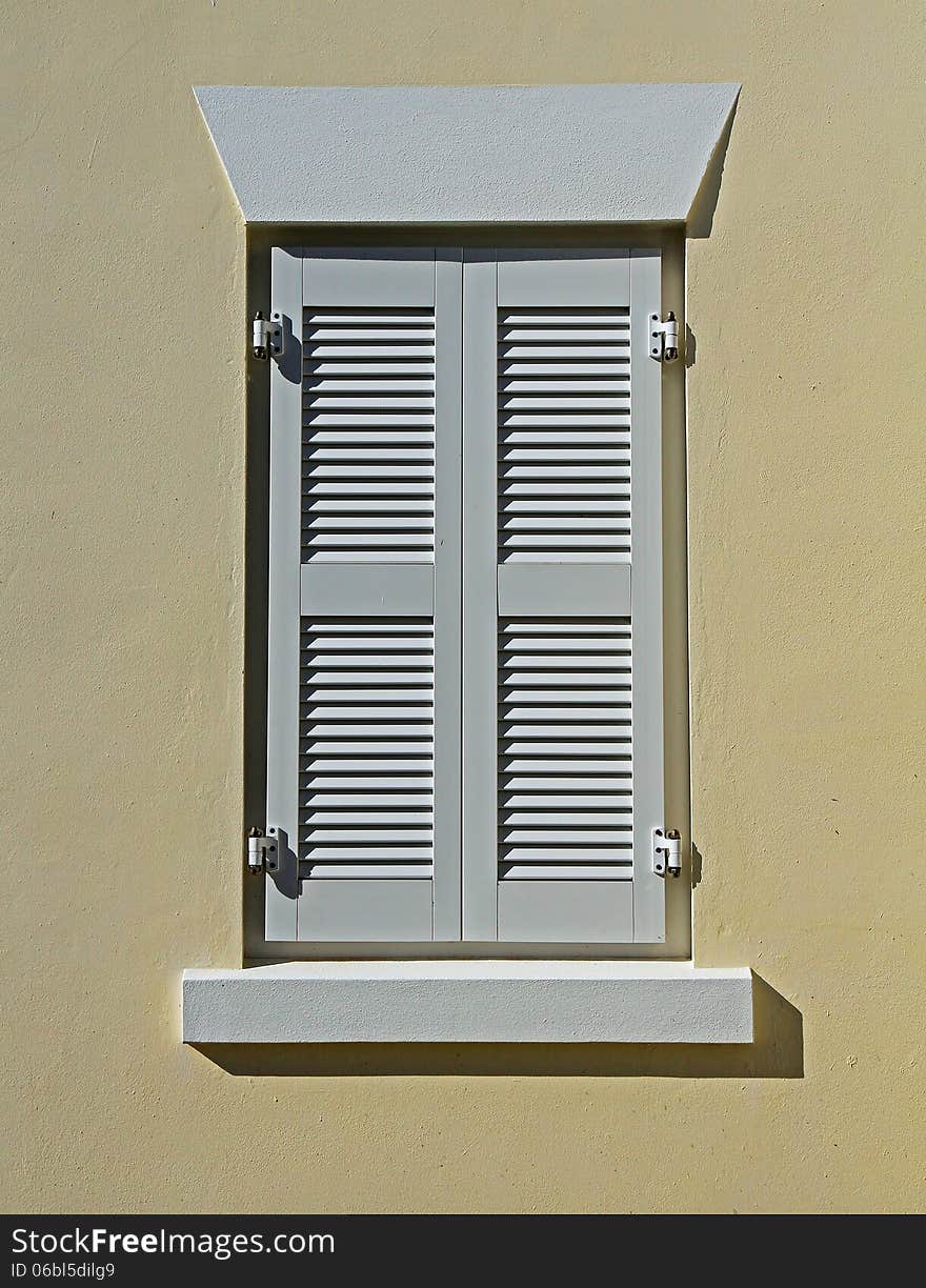Closed, white window shutters, against a cream wall. Closed, white window shutters, against a cream wall