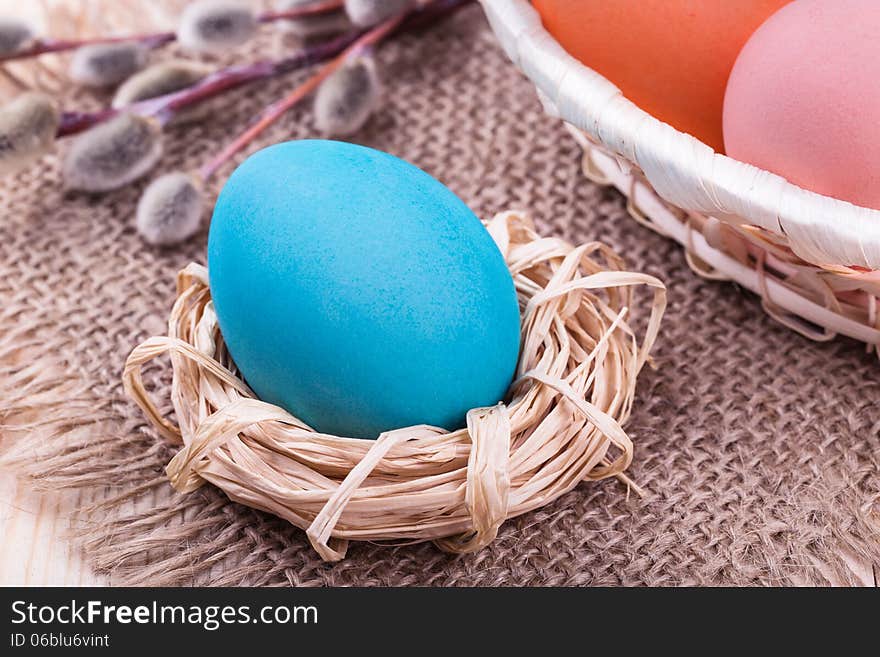 Easter egg in small nest with Easter basket and willow on wooden table