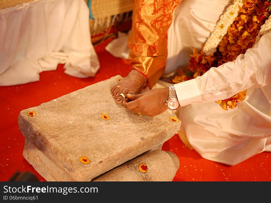 Bride groom is wearing a silver metti ring to the foot finger of bride placed on a grinding stone in a wedding function. Bride groom is wearing a silver metti ring to the foot finger of bride placed on a grinding stone in a wedding function