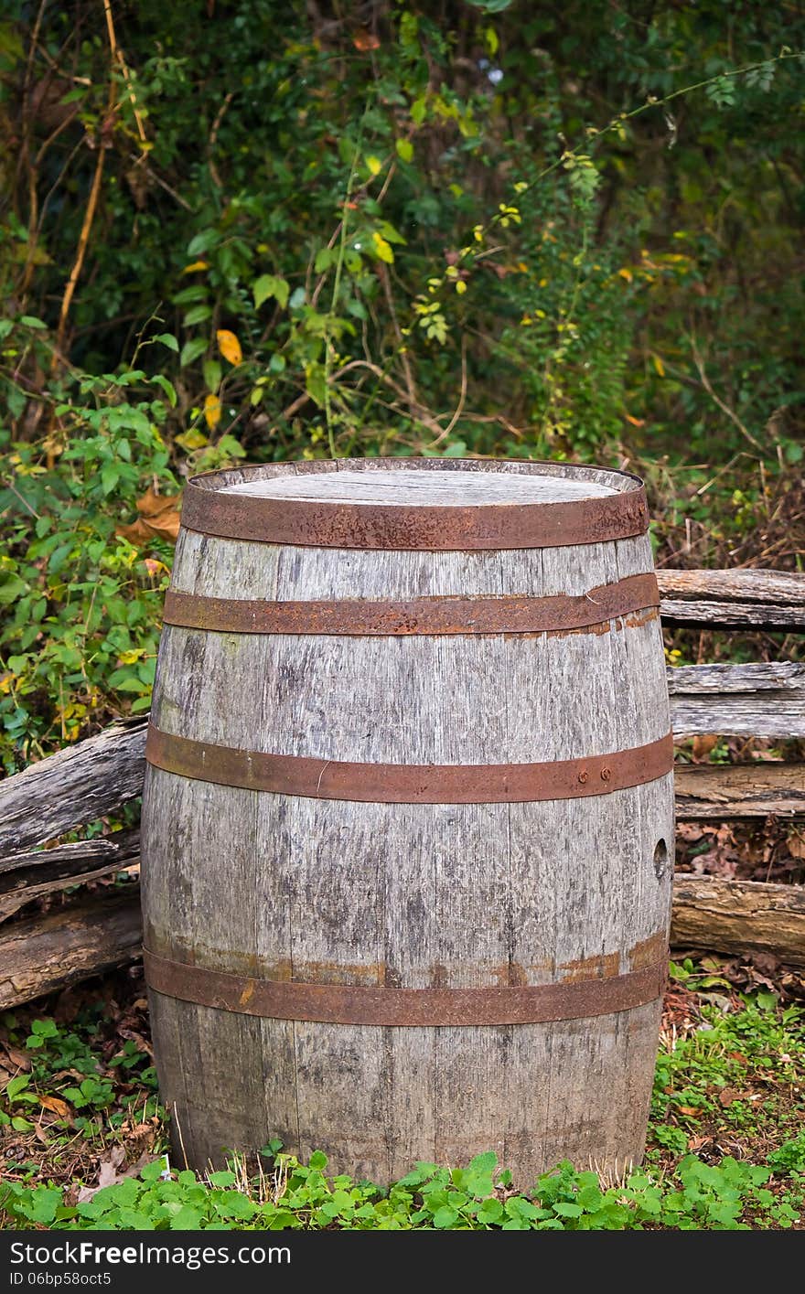 A vertical shot of an old and rustic barrel sitting in the corner of an old wooden fence. A vertical shot of an old and rustic barrel sitting in the corner of an old wooden fence.